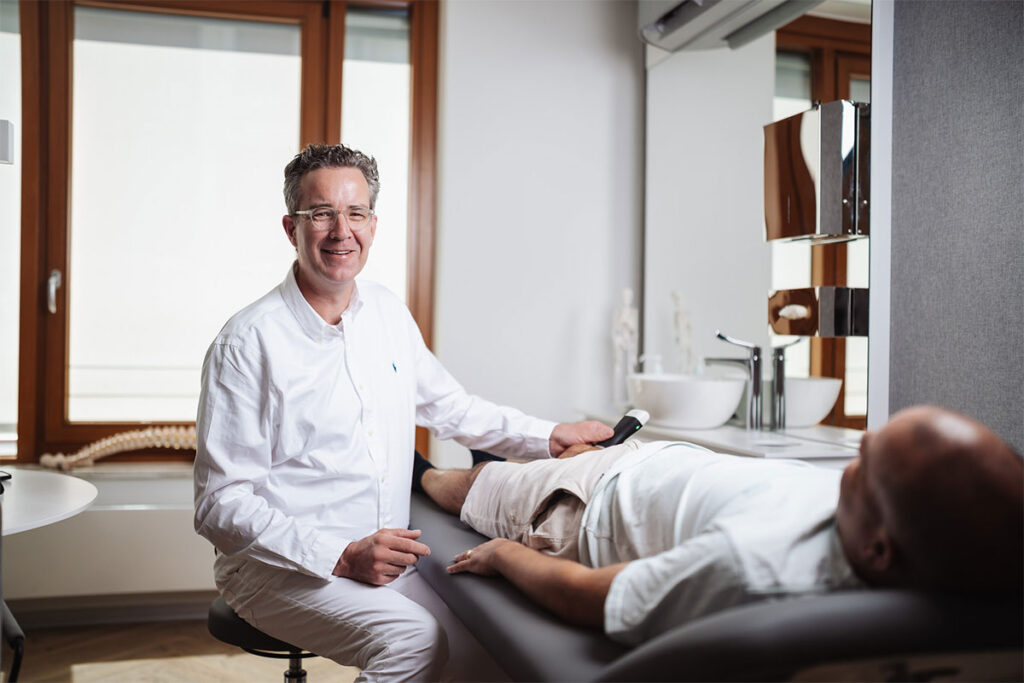 Dr. med. Stephan Meyer-Schwickerath untersucht einen Patienten auf der Behandlungsliege
